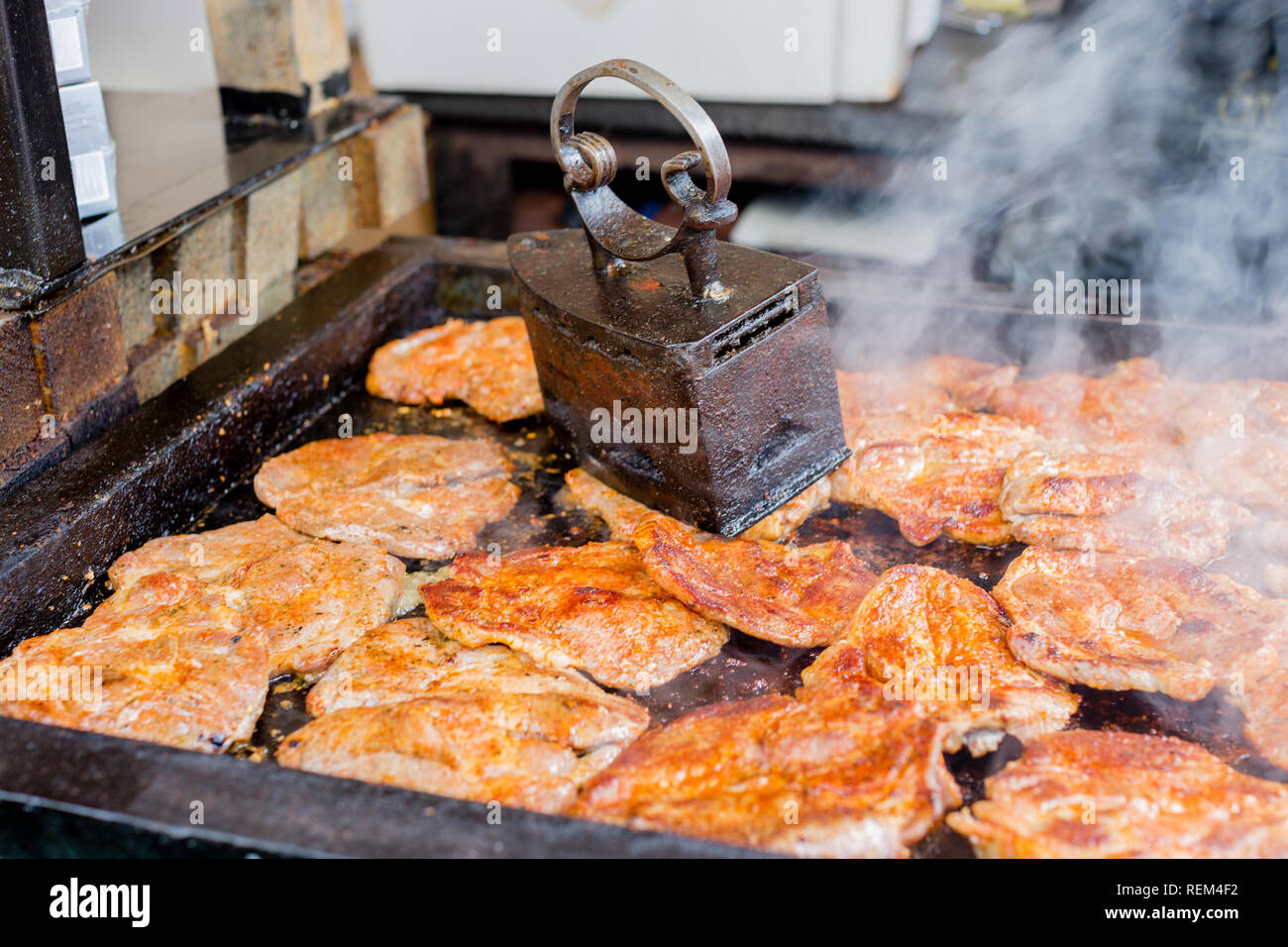 Succose bistecche di carne sul grill barbeque sotto vintage griglia ferro premere in street food festival Foto Stock