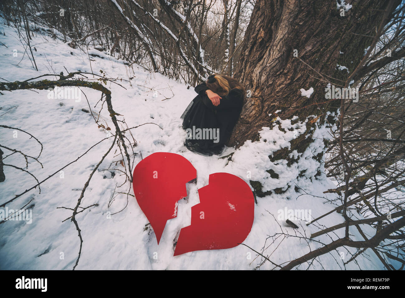 Premuto e cuori affranti donna poggiando su albero nella foresta in inverno. Foto Stock