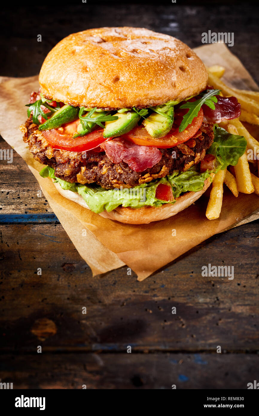 Avocado e guacamole burger su una spessa succosa carne patty e rabboccato con pancetta croccante servita con patatine fritte o rustico carta marrone Foto Stock