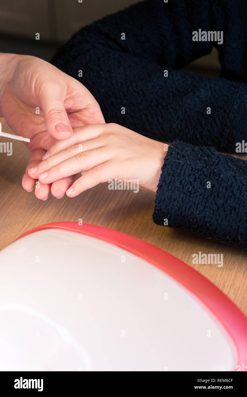 Close up di mani giovani ragazze mano mentre l'applicazione di smalto trasparente polacco, processo di manicure e la cura delle unghie - verticale Foto Stock