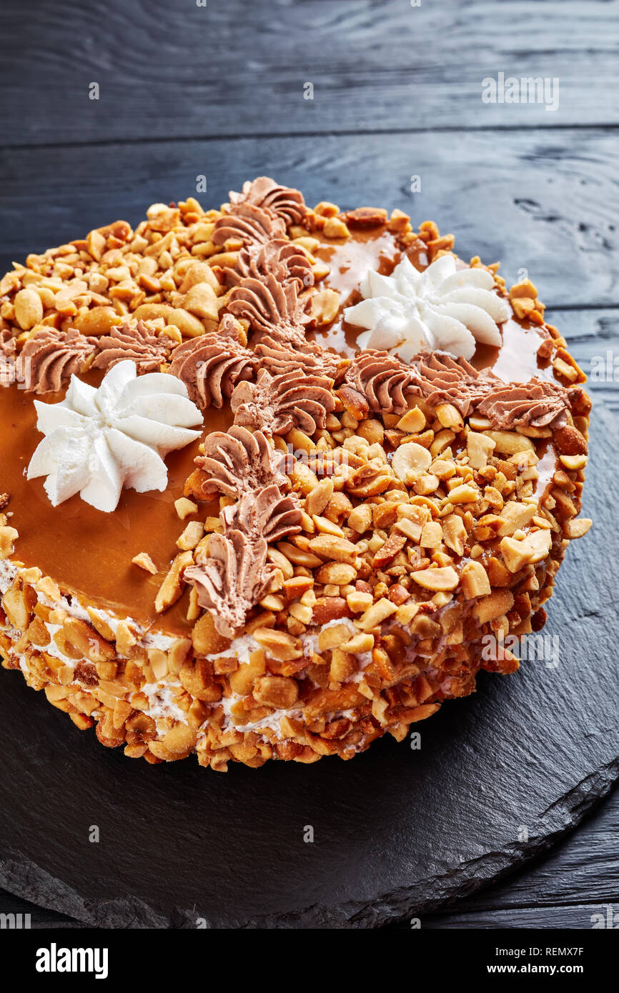 Torta di arachidi e rabboccato con cacao Burro di arachidi la panna e gli albumi rose su una lastra di pietra su una tavola di legno, verticale vista da sopra Foto Stock