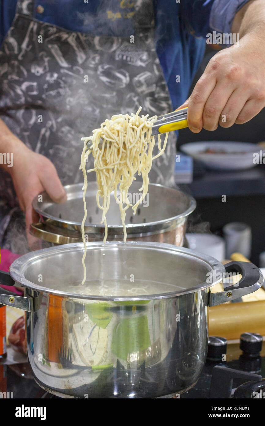 Lo Chef tiene fuori con la schiumarola fumante di noodle all'uovo da pan Foto Stock