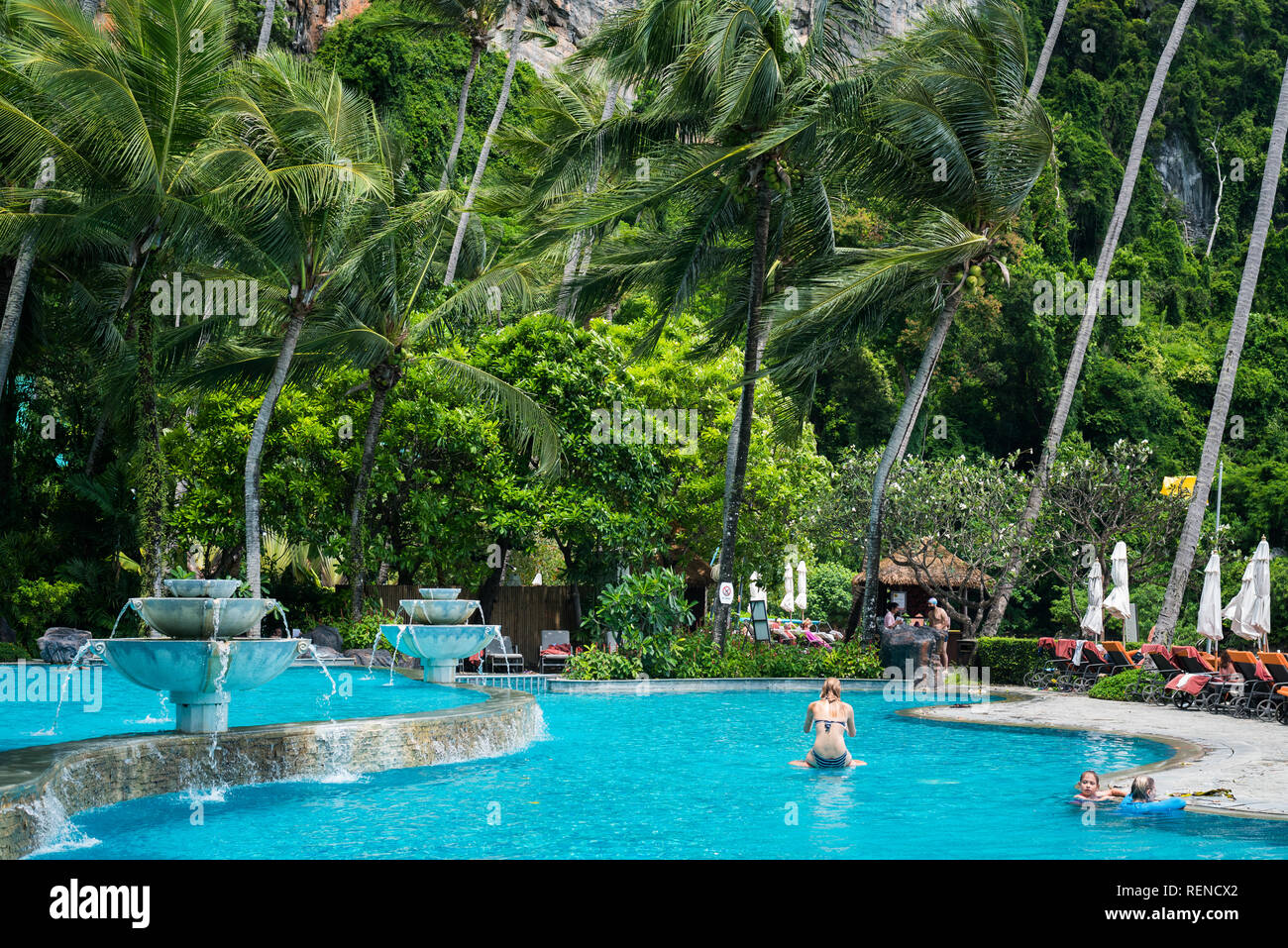 Ao Nang, Tailandia - 2 Luglio 2, 2018: una piscina blu con i turisti in esso sotto gli alberi di cocco che ondeggiano nel vento. Foto Stock