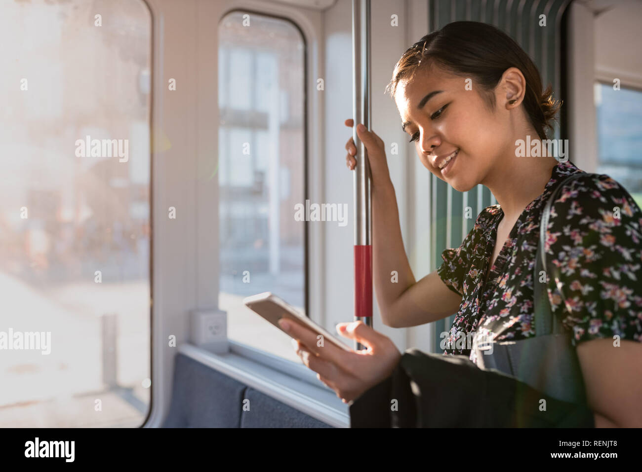 Sorridente imprenditrice asiatici a cavallo su un treno tramite il suo cellulare Foto Stock