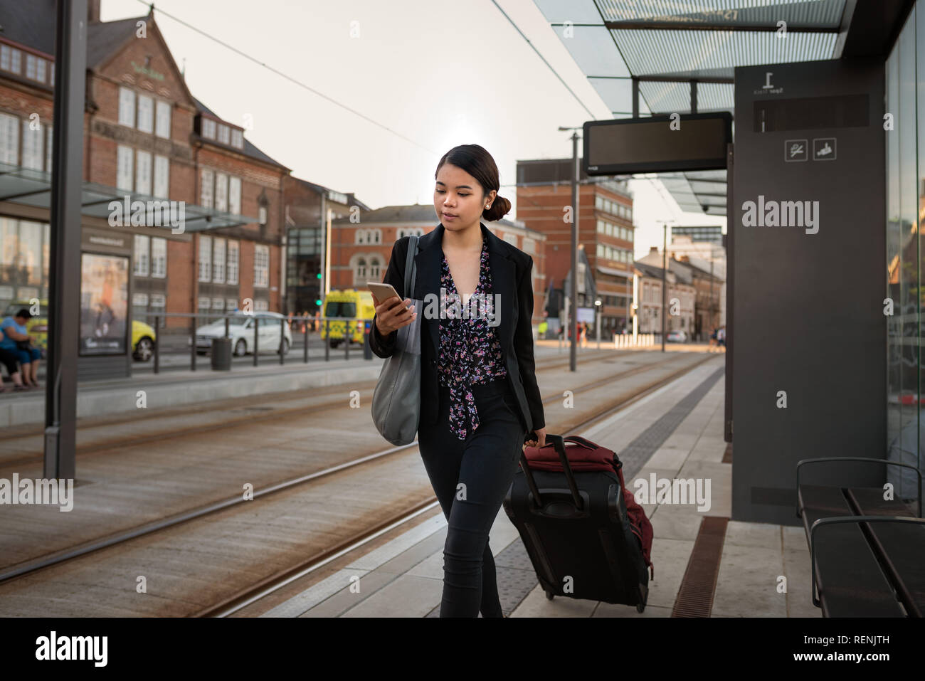 Imprenditrice asiatici in attesa con i suoi bagagli utilizzando un telefono cellulare Foto Stock