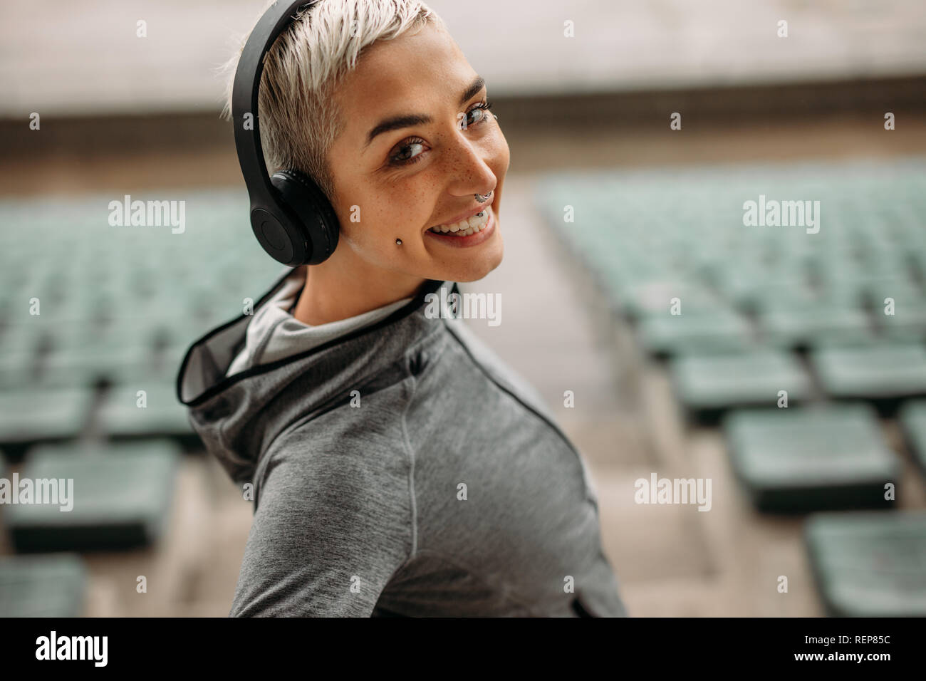 Vista laterale in prossimità di una donna in piedi sulle scale di uno stadio. Ritratto di una donna sorridente in felpa e cuffie senza fili nelle gabbie di Foto Stock