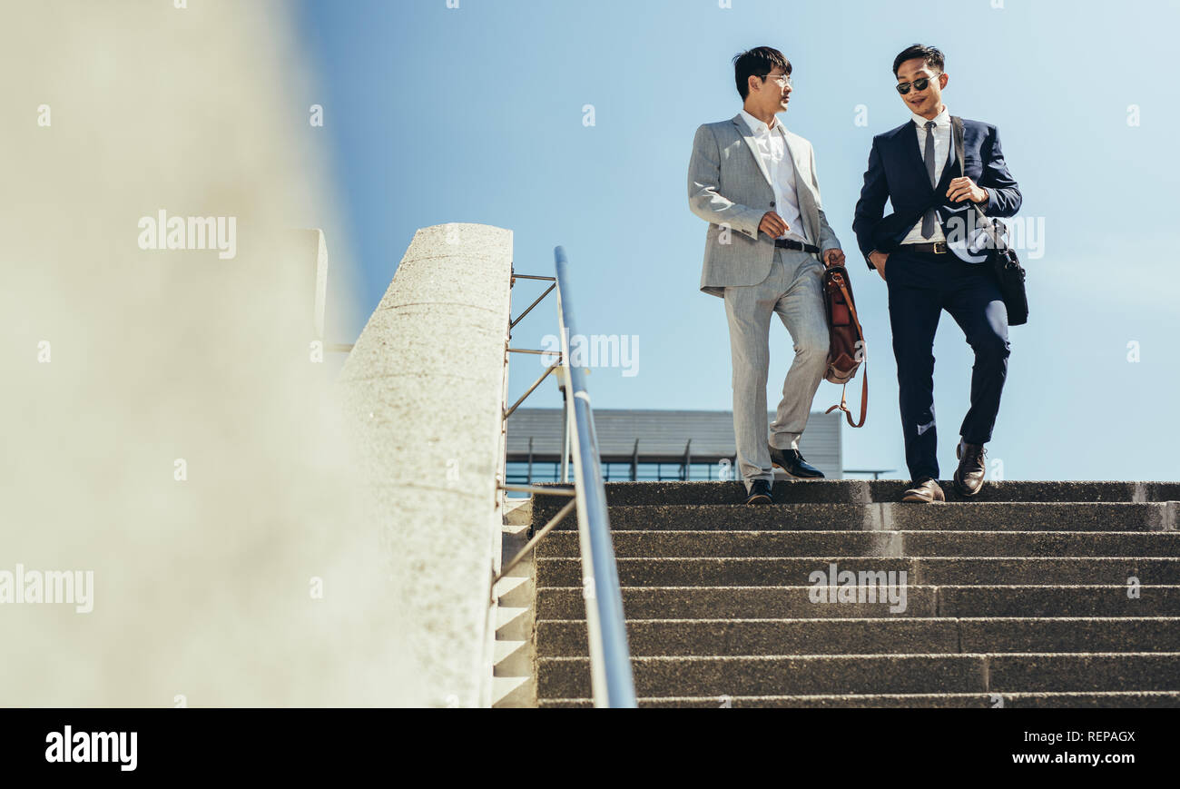 Due partner commerciali insieme a piedi giù per le scale nella città. Il coreano uomini d' affari percorrendo a piedi le fasi e parlare. Foto Stock