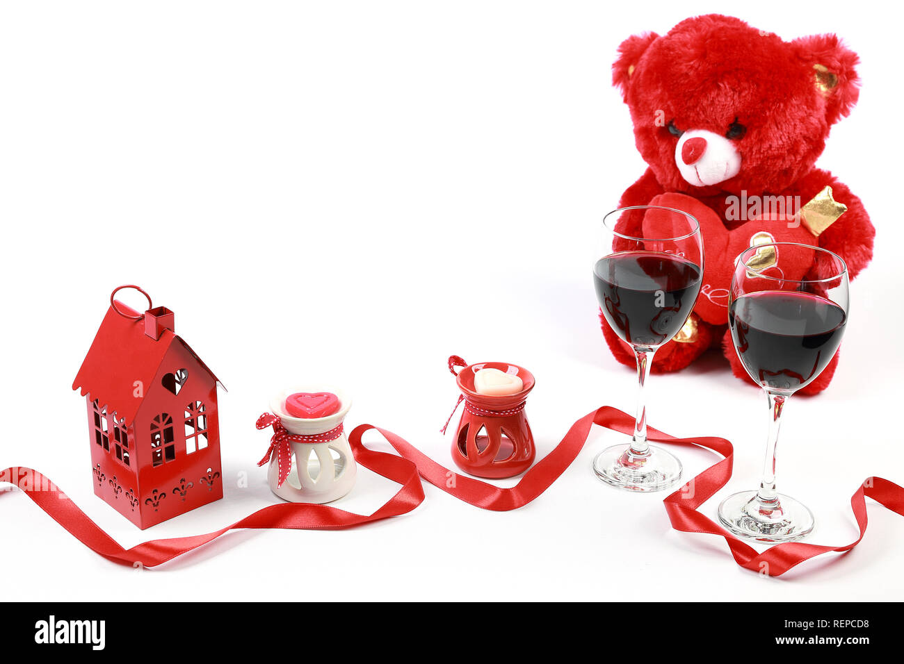 Il giorno di San Valentino del concetto. Red orsacchiotto con un bicchiere di vino rosso a forma di cuore candela con un nastro rosso e rose rosse isolato su sfondo bianco. Foto Stock