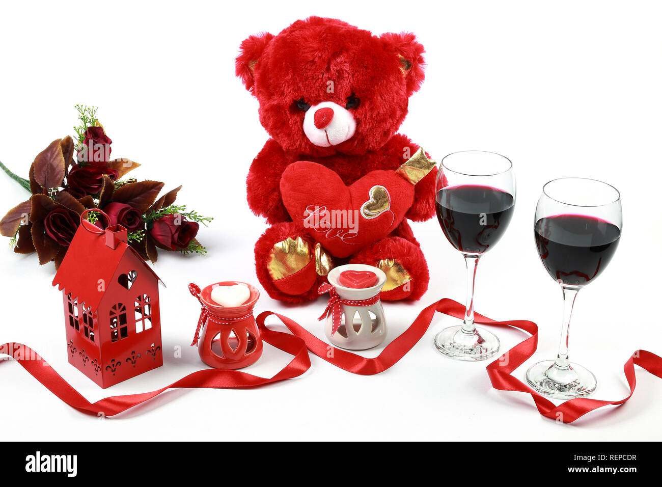 Il giorno di San Valentino del concetto. Red orsacchiotto con un bicchiere di vino rosso a forma di cuore candela con un nastro rosso e rose rosse isolato su sfondo bianco. Foto Stock