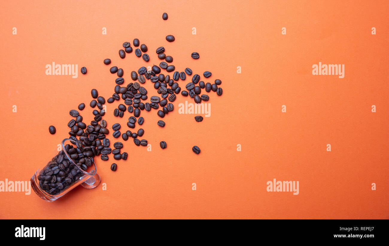 I chicchi di caffè e un bicchiere di vetro, sul colore arancione brillante background, copia spazio, vista dall'alto Foto Stock