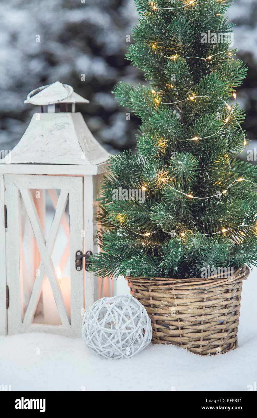 White Lanterna di legno con cera bianca candela accesa e piccole Natale abete con micro luci a led in rattan di colore marrone pentola floreale in snow, innevate di abeti Foto Stock