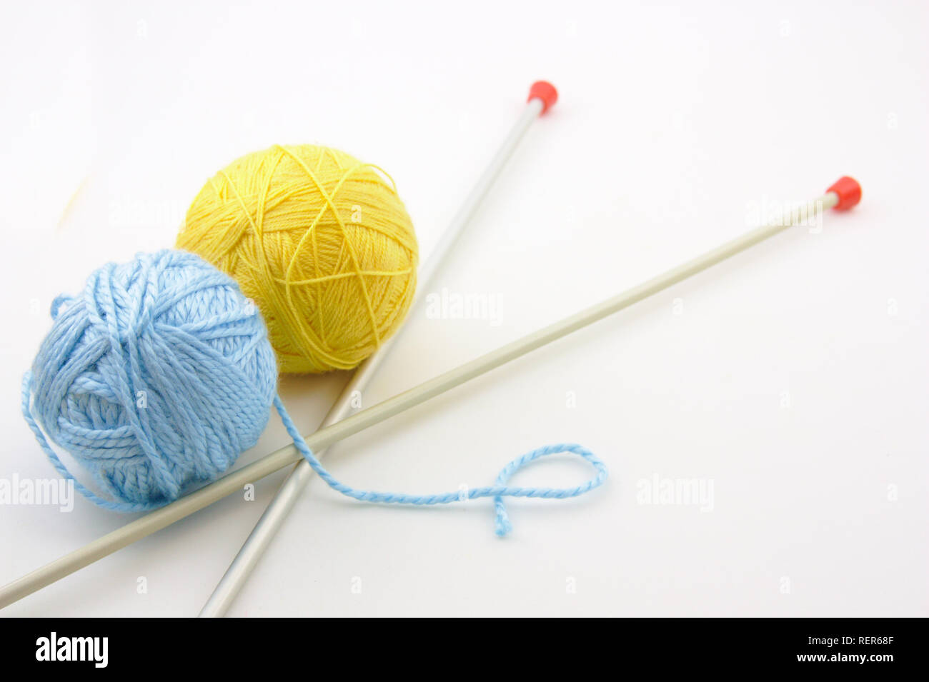 Due palle di lana, uno giallo e l'altra blu, accanto agli aghi di tessitura Foto Stock