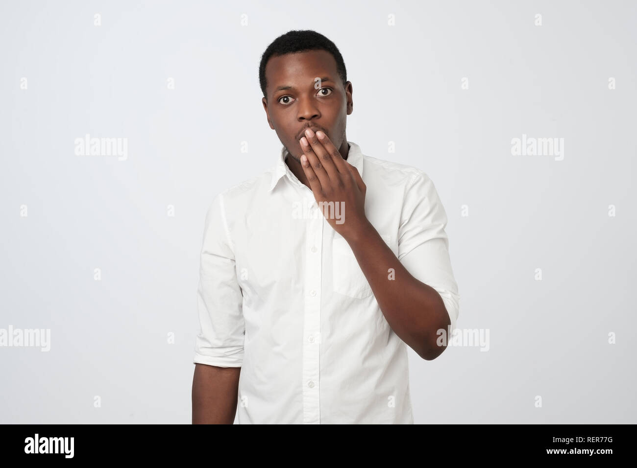 Scioccato giovane africano in abbigliamento formale che copre la bocca con la mano. Foto Stock