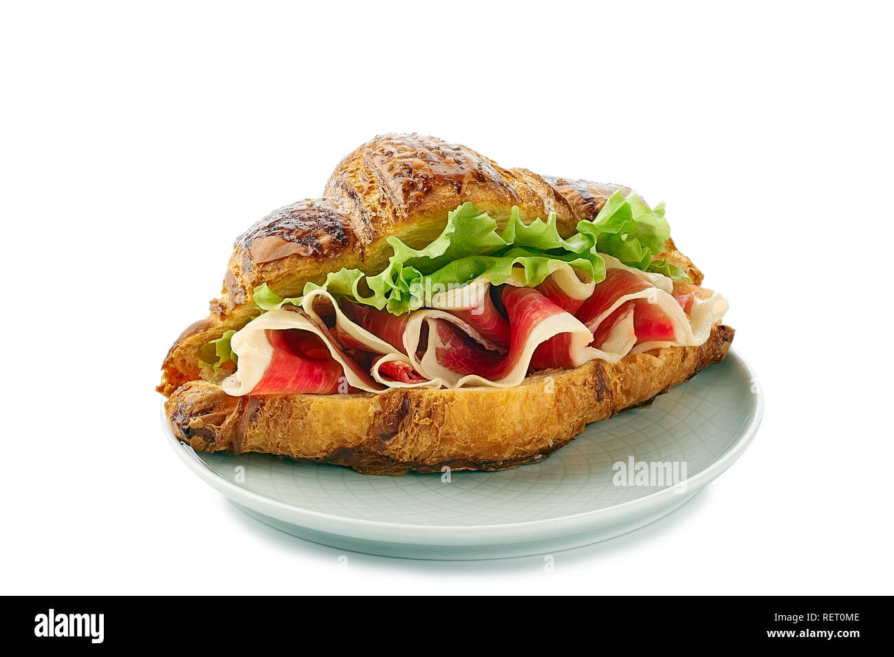 Piastra con croissant sandwich con prosciutto di prosciutto e lattuga su bianco Foto Stock