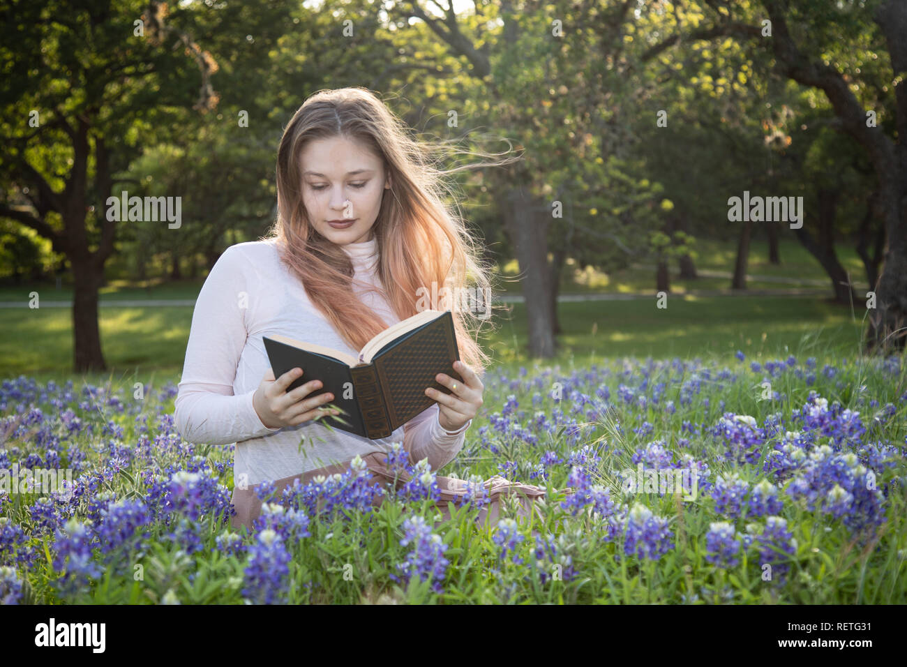 Ragazza la lettura di un libro in bluebonnet fiori Foto Stock