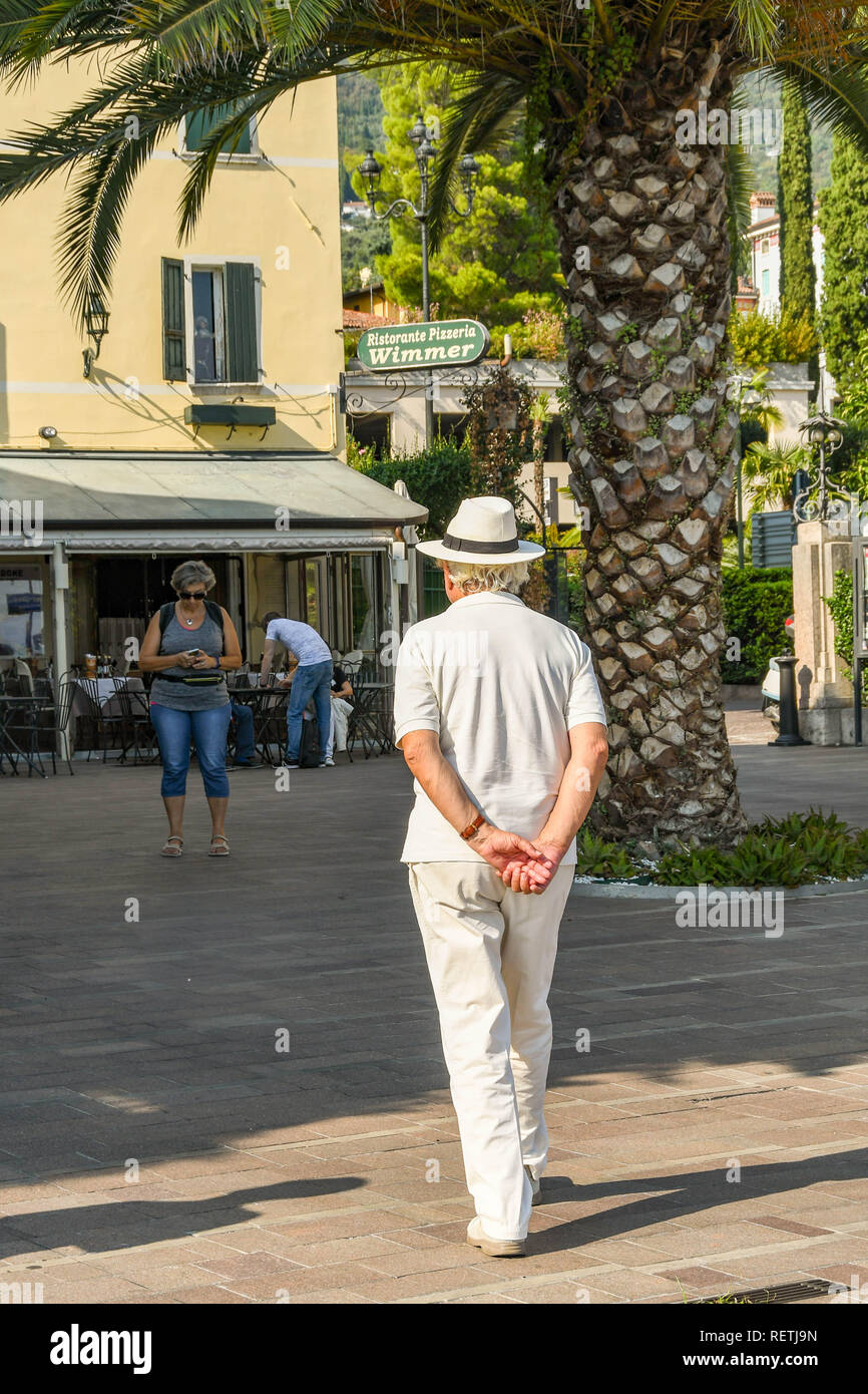 GARDONE RIVIERA, Italia - Settembre 2018: Persona con cappello per il sole passeggiando per la piazza della città di Gardone Riviera sul lago di Garda con le sue mani giunte Foto Stock