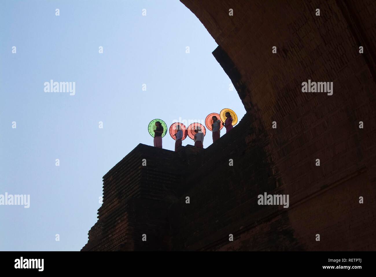 Giovani donne birmane con ombrelloni colorati in piedi su una parete del tempio, Bagan, Myanmar Foto Stock