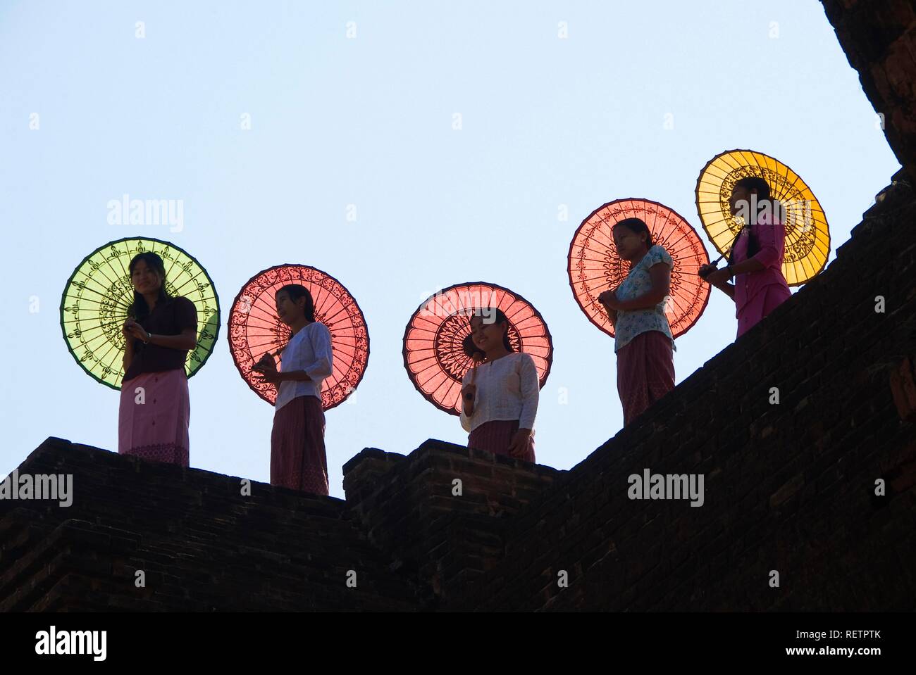 Giovani donne birmane con ombrelloni colorati in piedi su una parete del tempio, Bagan, Myanmar Foto Stock