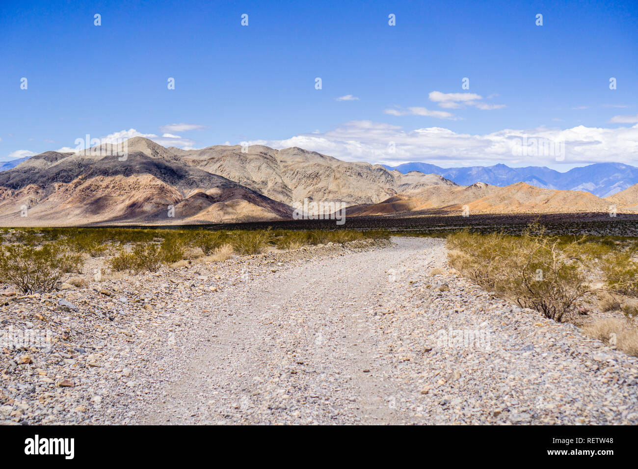 Viaggia su una strada sterrata attraverso una zona remota del Parco Nazionale della Valle della Morte; le montagne e il cielo blu in background; California Foto Stock