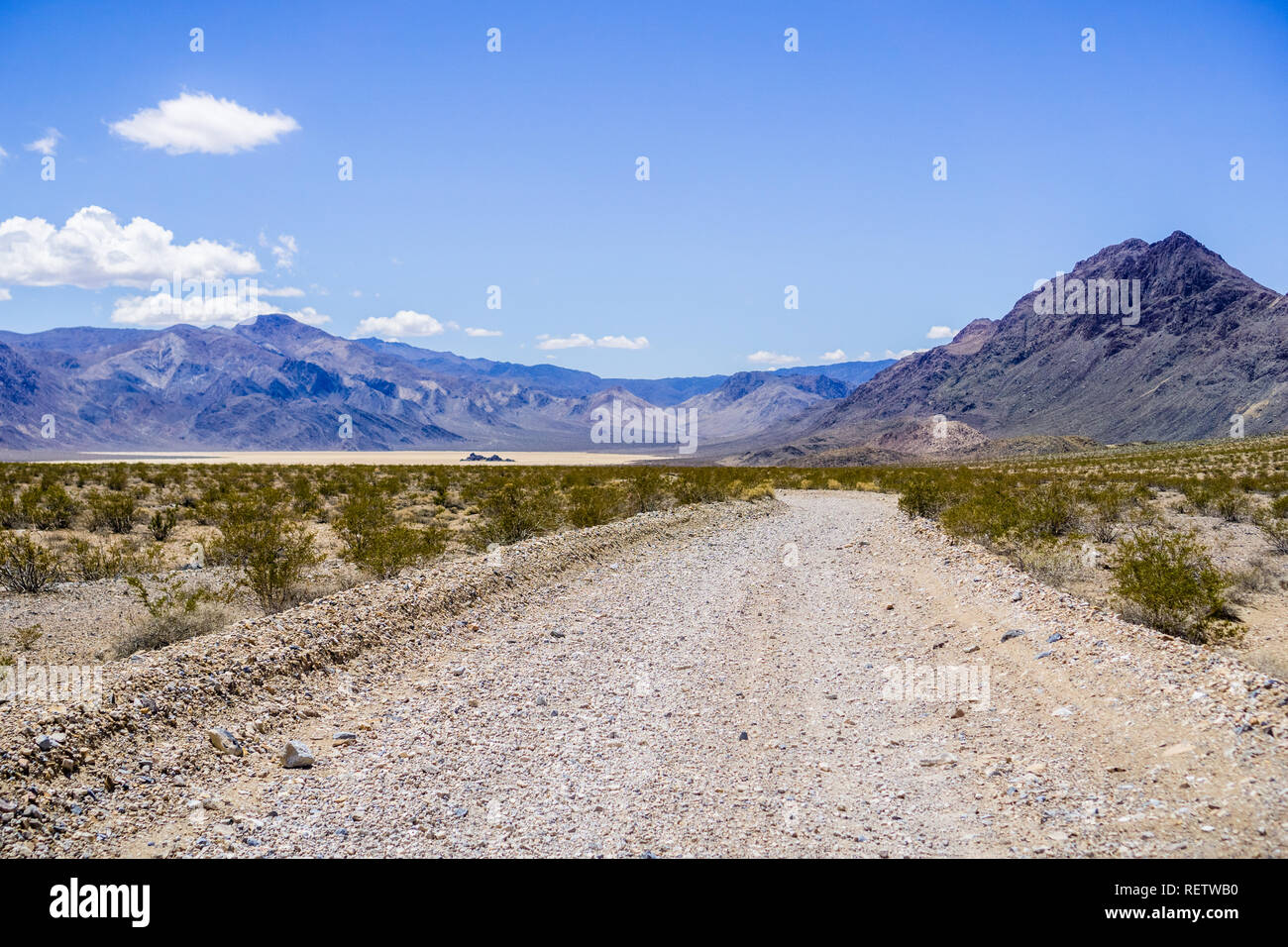 Viaggia su una strada sterrata attraverso una zona remota del Parco Nazionale della Valle della Morte; Racetrack Playa, delle montagne e del cielo blu in background; Californ Foto Stock