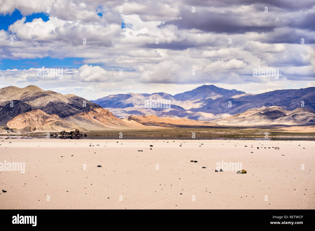 Spostando rocce sparse attorno alla superficie del Racetrack Playa; le montagne e le nuvole paesaggio sullo sfondo; Parco Nazionale della Valle della Morte, Californ Foto Stock