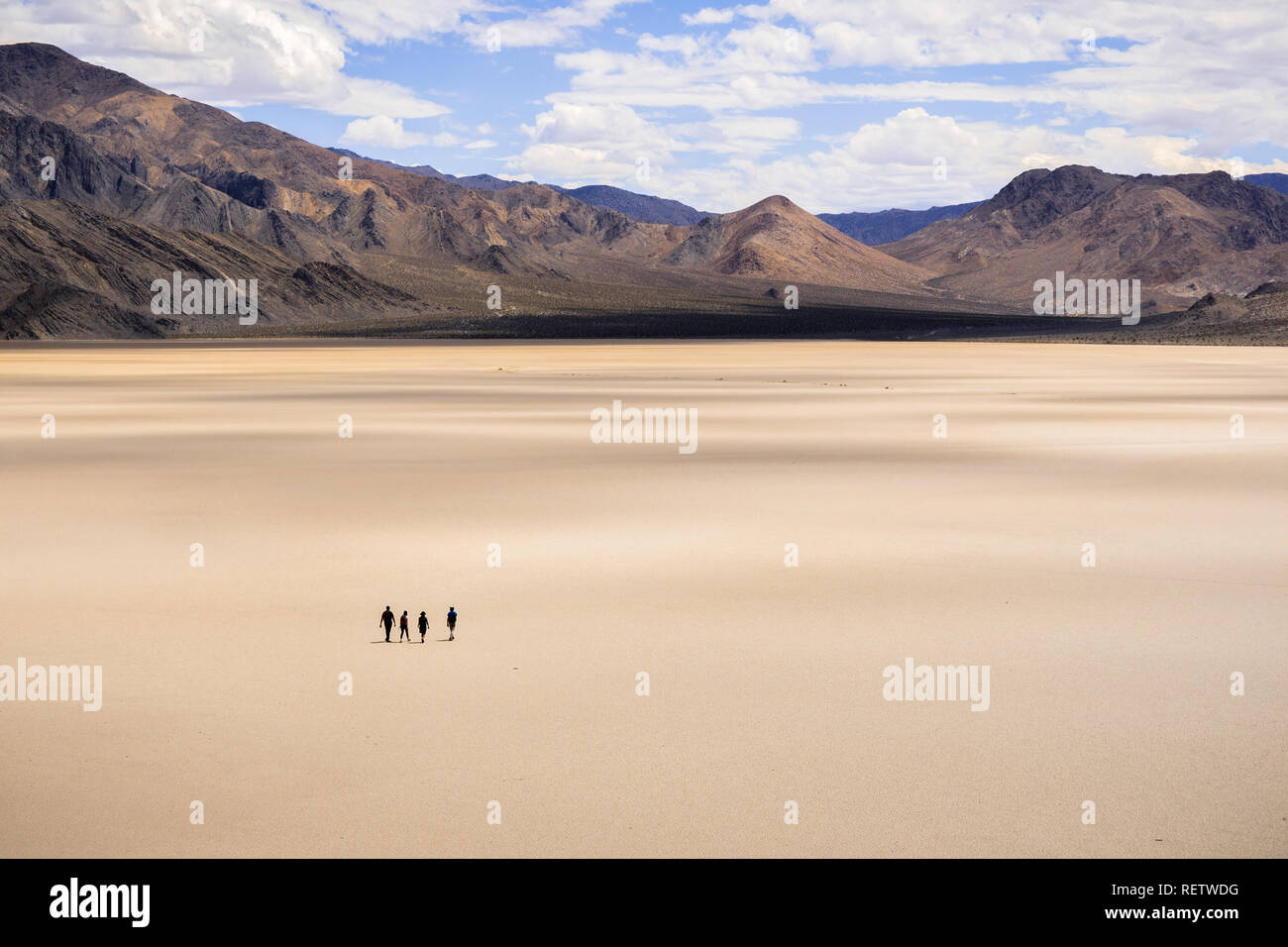 Un gruppo di amici a piedi attraverso la superficie della pista Playa in una giornata di sole; le montagne e nuvole bianche in background; Death Valley Nazione Foto Stock