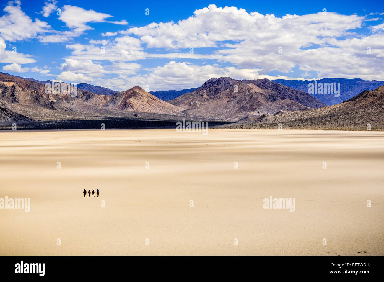 Un gruppo di amici che fanno la loro strada attraverso la superficie della pista Playa in una giornata di sole; le montagne e nuvole bianche in background; morte Vall Foto Stock