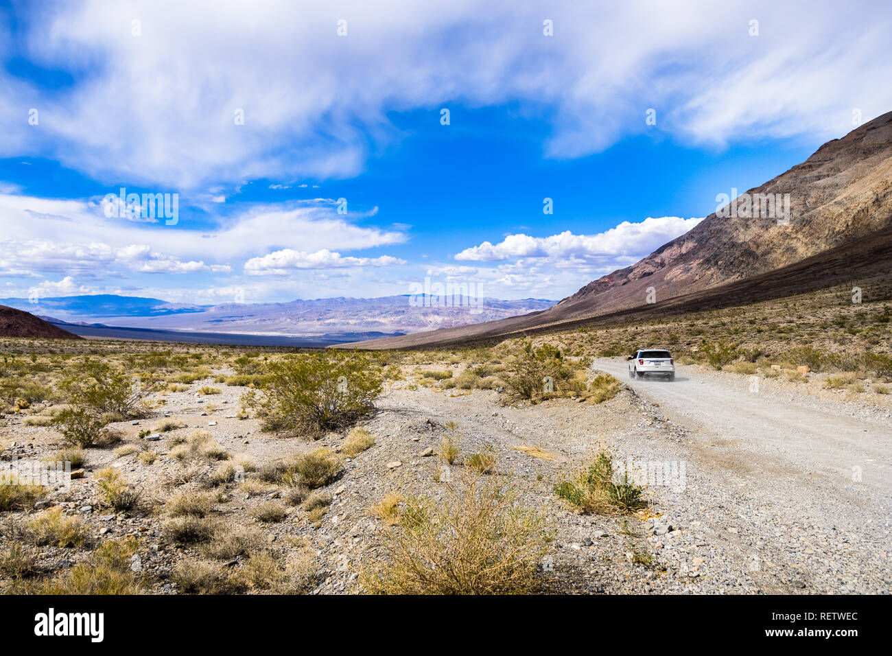 Viaggia su una strada sterrata attraverso una zona remota del Parco Nazionale della Valle della Morte; montagne, cielo blu e nuvole bianche in background; California Foto Stock