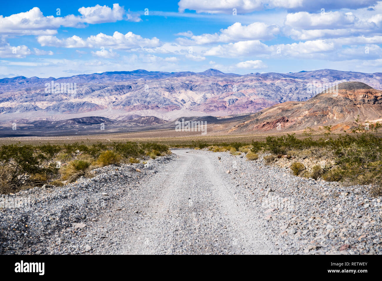 Viaggia su una strada sterrata attraverso una zona remota del Parco Nazionale della Valle della Morte; montagne, cielo blu e nuvole bianche in background; California Foto Stock