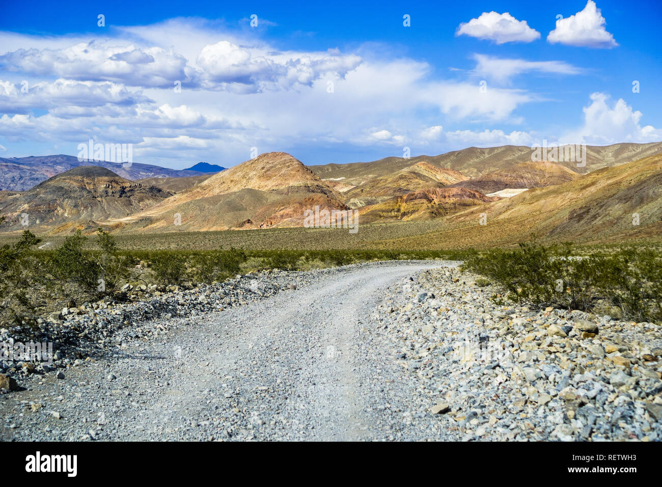 Viaggia su una strada sterrata attraverso una zona remota del Parco Nazionale della Valle della Morte; montagne, cielo blu e nuvole bianche in background; California Foto Stock