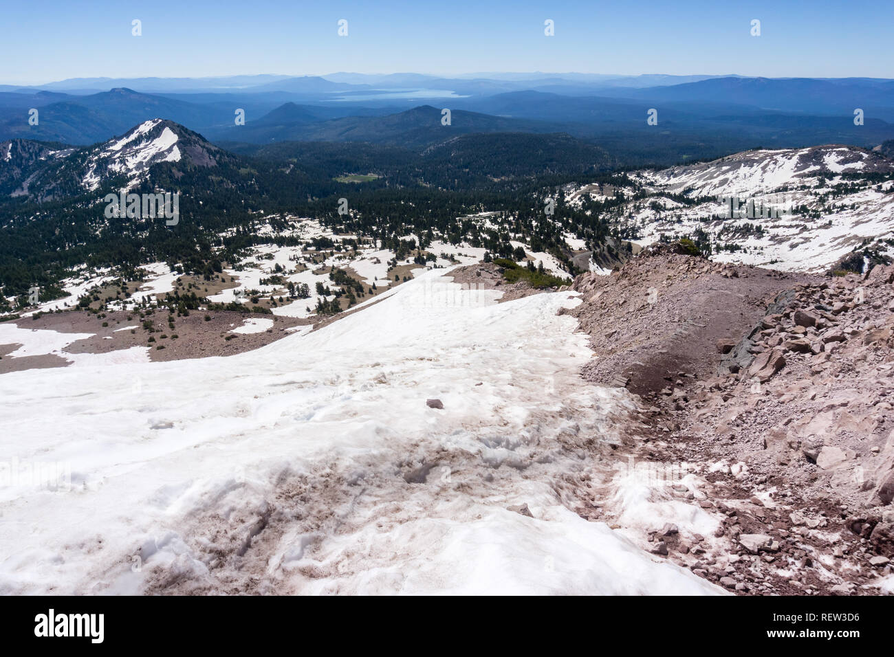 Trekking in alta quota il sentiero a picco Lassen parzialmente coperto di neve su una soleggiata giornata estiva; lago Almanor visibile in background; vulcanico di Lassen Nat Foto Stock