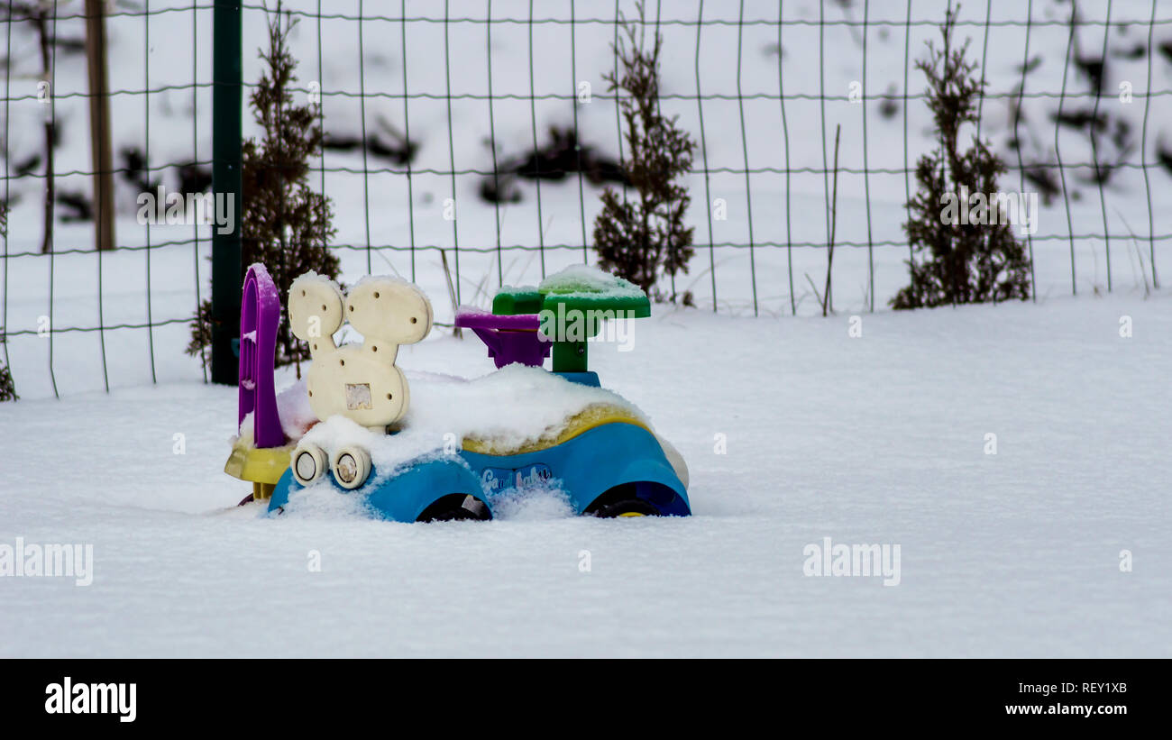 Blu, giallo e viola i bambini modellini di auto parcheggiate nella neve dopo una tempesta di neve con la neve su di essi Foto Stock