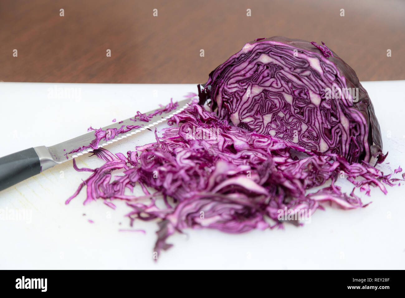 Rosso tritato Coleslaw su bianco e lo sfondo in legno con coltello da cucina sul lato. Culinario vista superiore Foto Stock