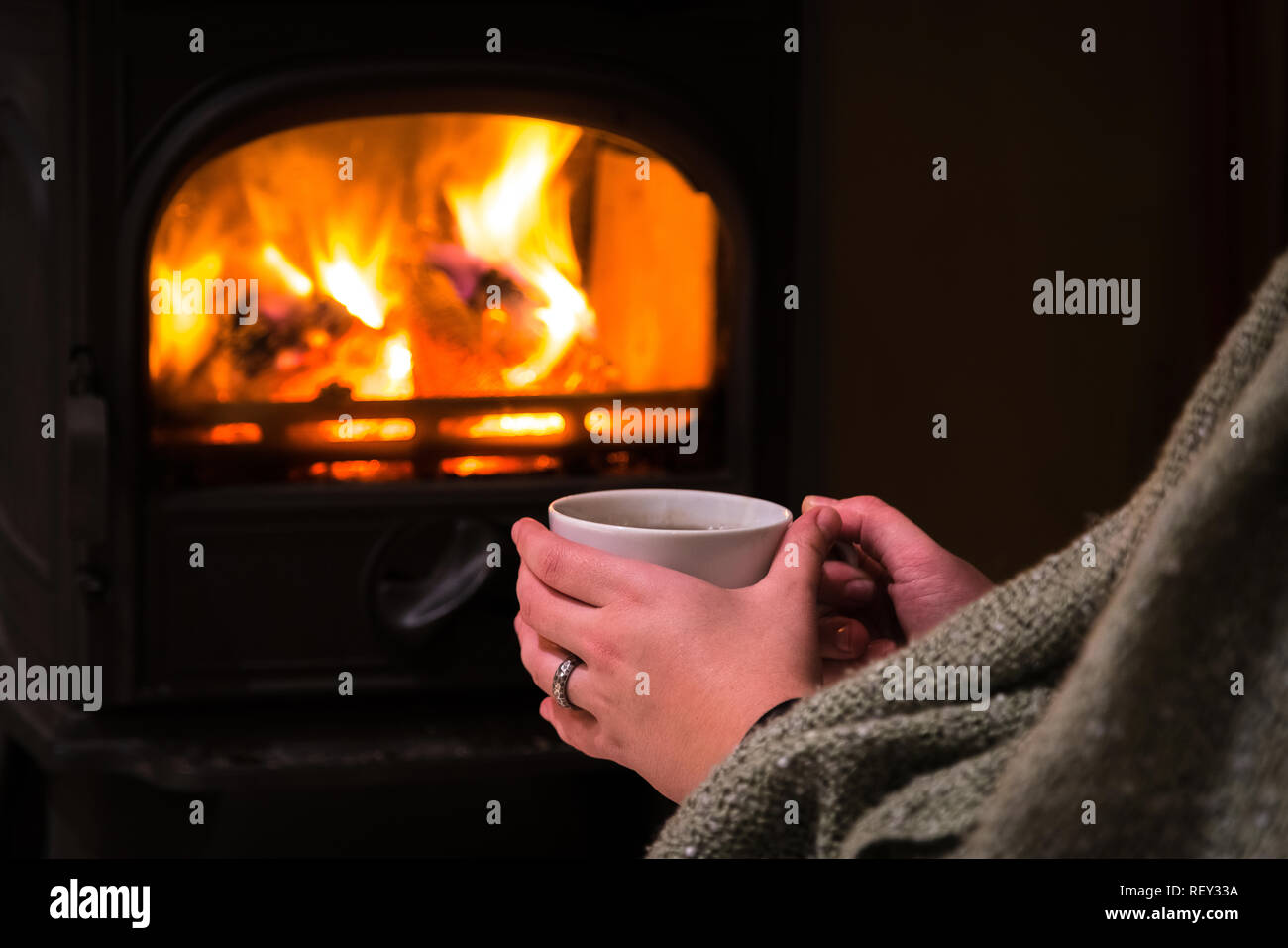 Donna con una calda tazza di ghiaccio davanti al camino. La masterizzazione di camino con tronchi di legno che brucia in background. Luce calda, romantico, natale Foto Stock