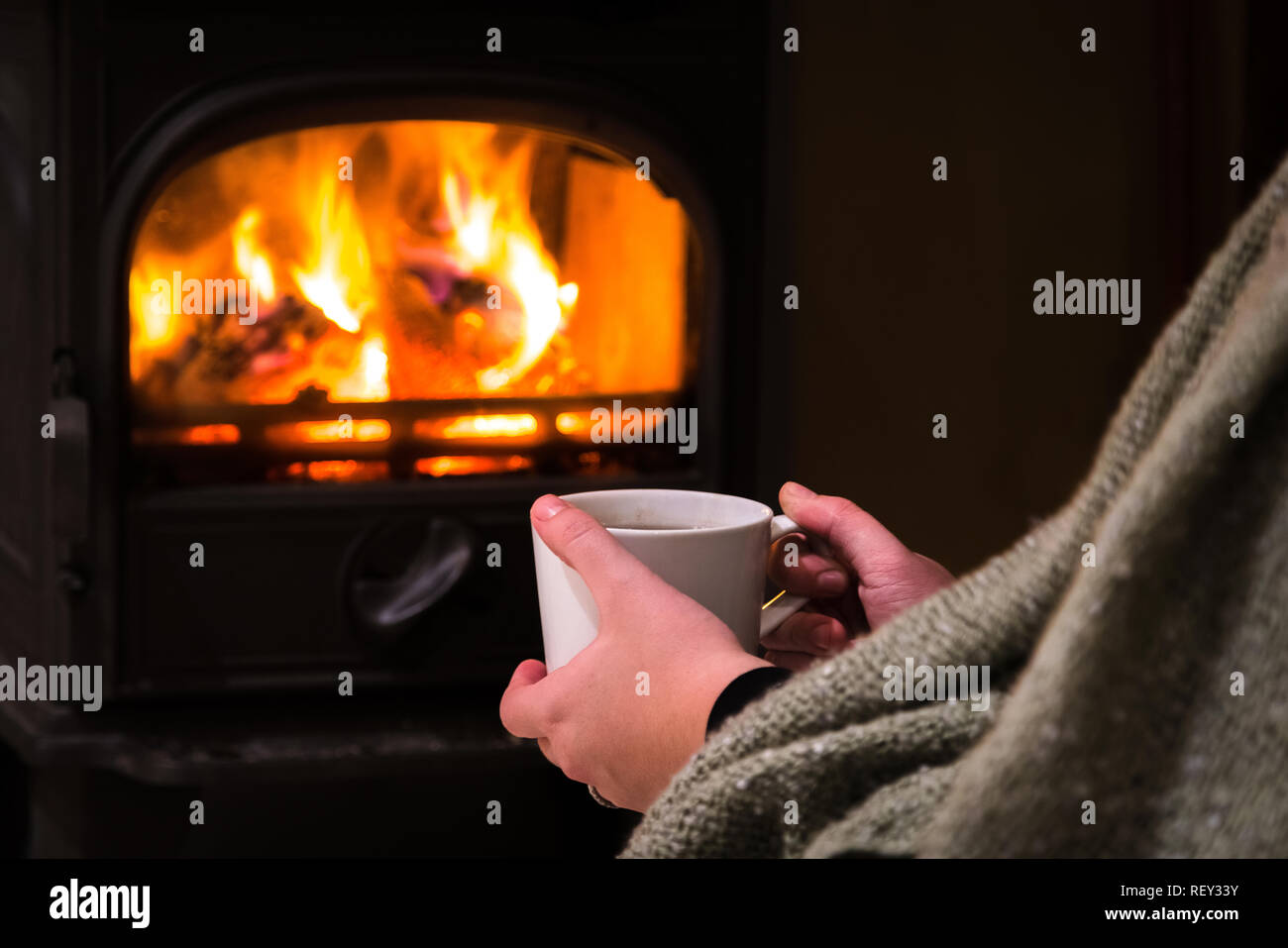Donna con una calda tazza di ghiaccio davanti al camino. La masterizzazione di camino con tronchi di legno che brucia in background. Luce calda, romantico, natale Foto Stock