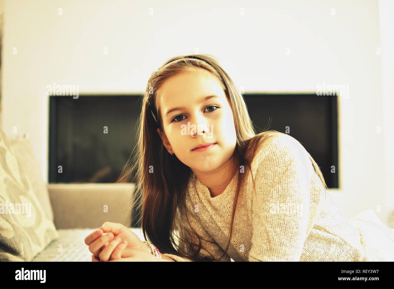 Ritratto di una bionda sorridente caucasico bianco 9 anni ragazza seduta vicino a un divano. Il bambino ha i capelli lunghi. Vista frontale, il fuoco selettivo. Foto Stock