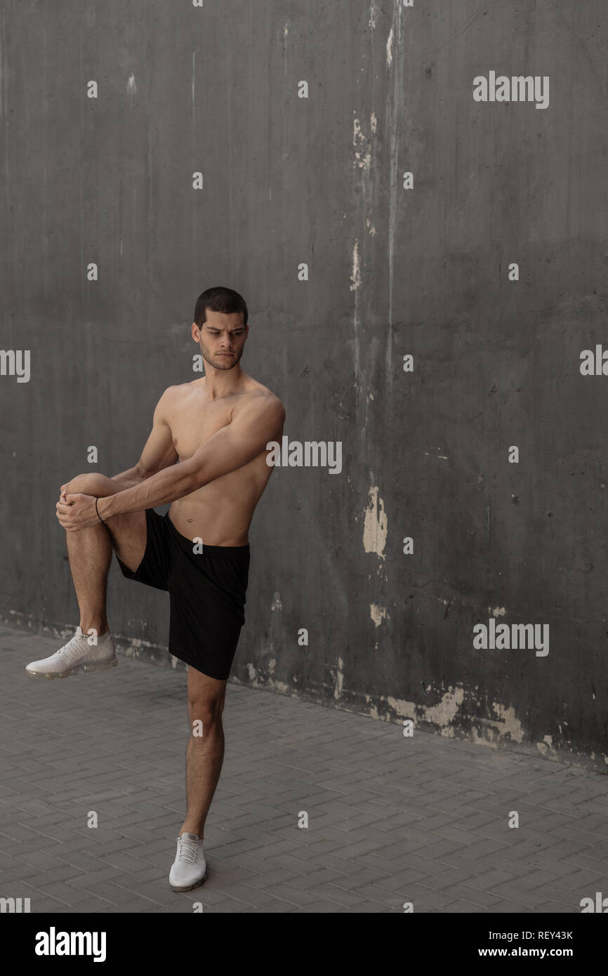 Bello e atletico uomo riscaldamento stretching prima della formazione, con pareti grigie in background. Uno stile di vita sano e sportswear pubblicità. Foto Stock