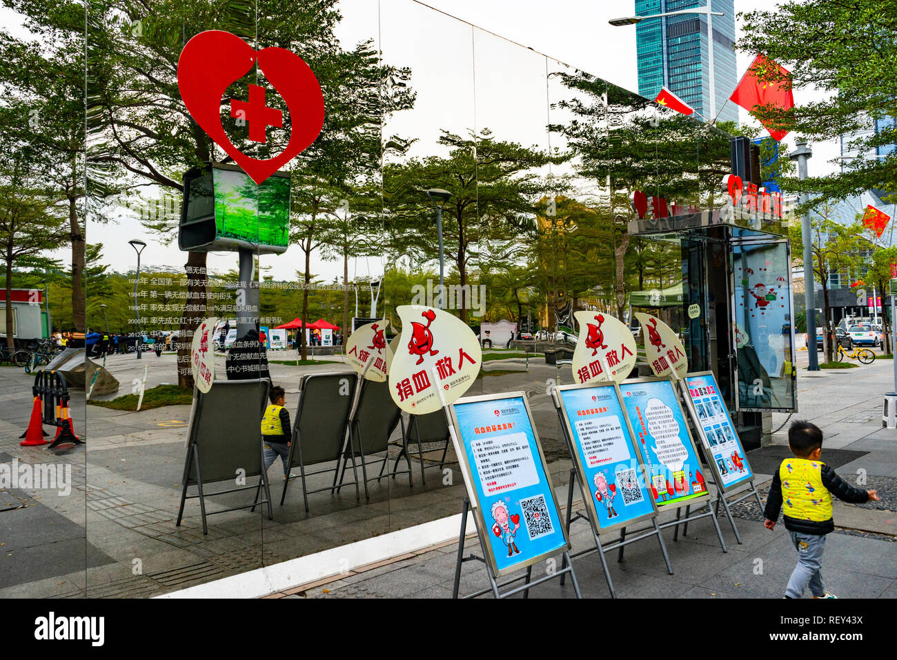Ragazzo oltrepassando la banca del sangue stazione (Shenzhen Centro di sangue) con facciata riflettente in Shenzhen, Cina Foto Stock
