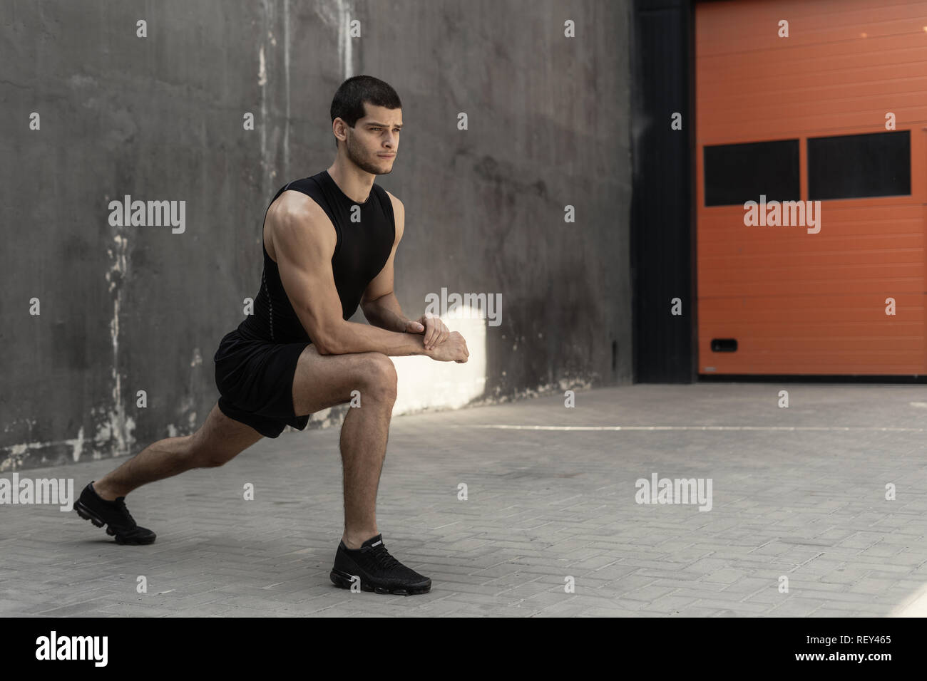 Bello e atletico uomo riscaldamento stretching prima della formazione, con pareti grigie in background. Uno stile di vita sano e sportswear pubblicità. Foto Stock