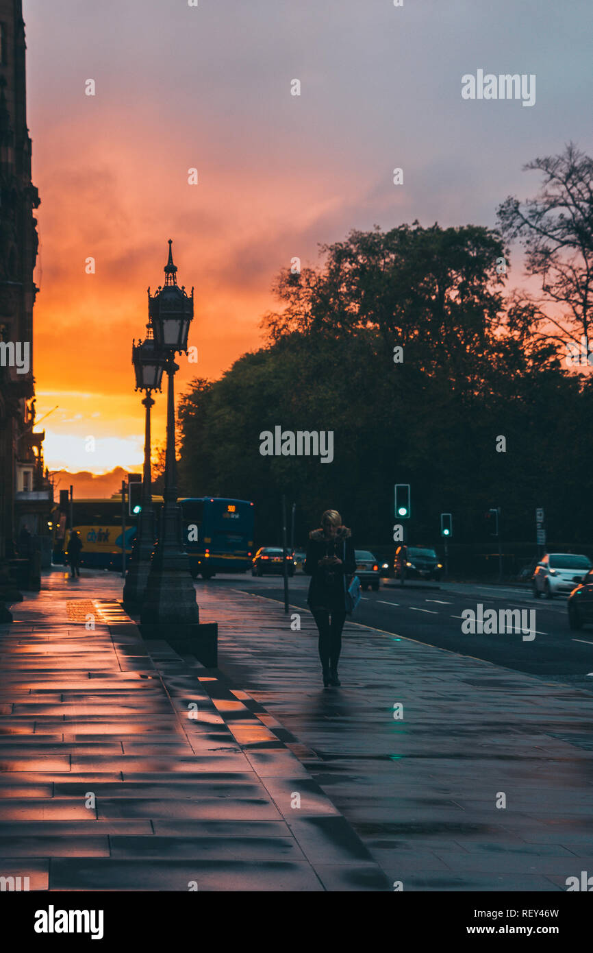 Donna con cuffie a camminare in una strada bagnata al tramonto a Edimburgo. La vita in città Foto Stock