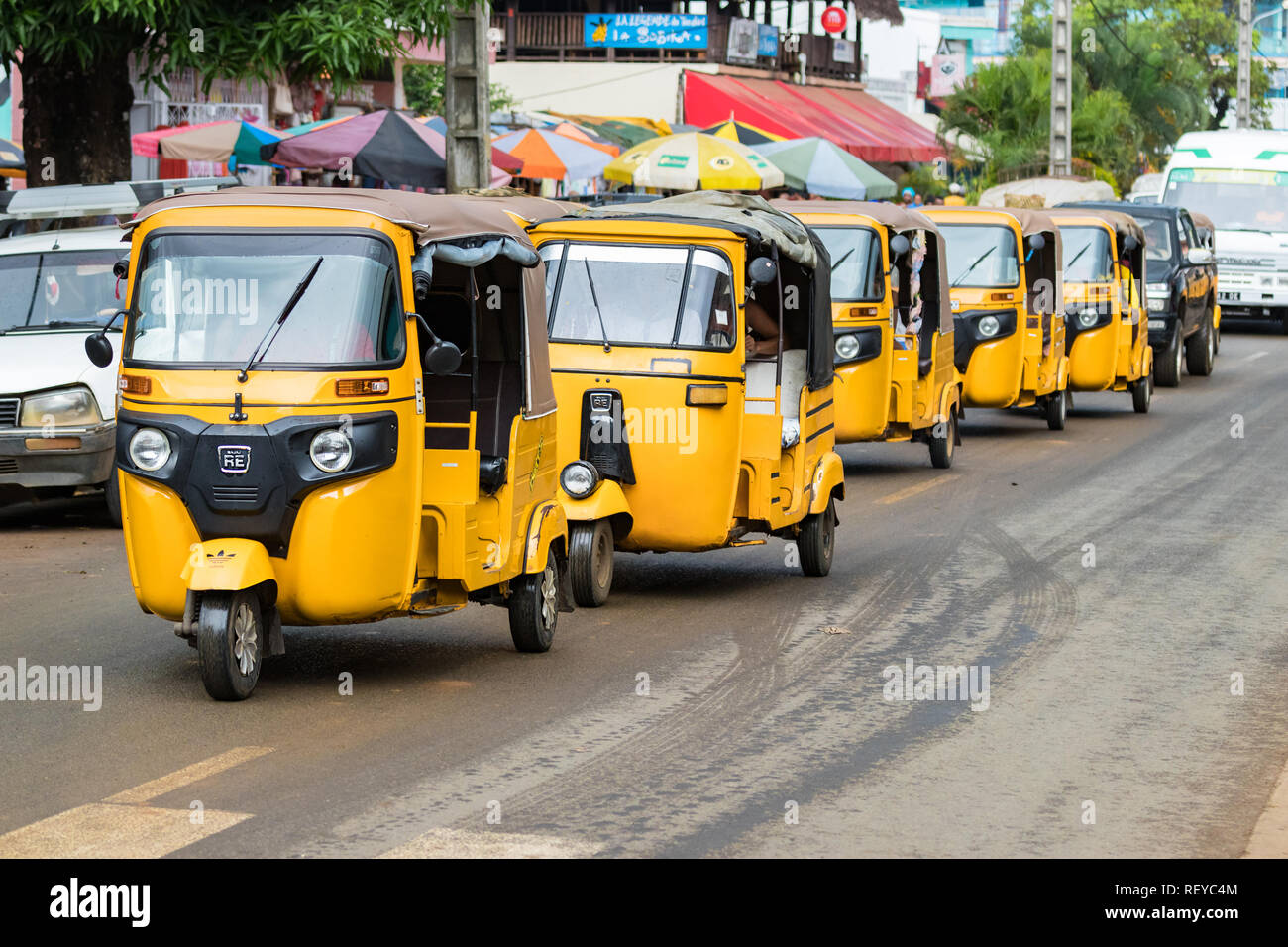 Nosy Be, Madagascar - Gennaio 17th, 2019: Linea di colori gialli Tuk-Tuks in una riga, un taxi triciclo motorizzato a Nosy Be, Madagascar. Foto Stock