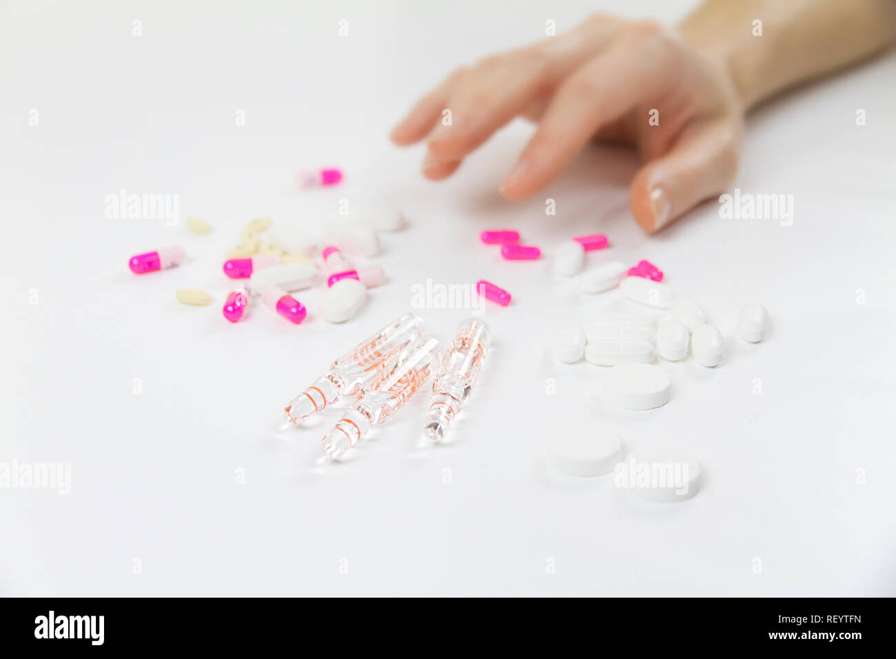 Dipendenza da farmaci e droghe in tempi moderni: close-up shot di una giovane donna sulla mano per afferrare vari compresse e fiale sul tavolo e white bac Foto Stock