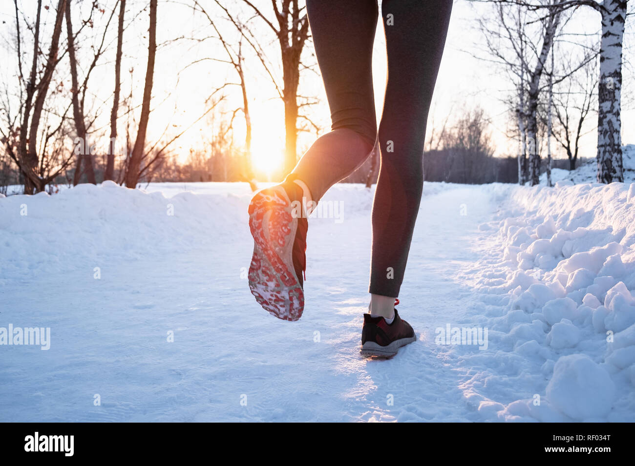 Il jogging all'aperto in inverno concetto. Le gambe di una persona di sesso femminile che corre lungo la strada innevata sulla bella giornata fredda, sparato contro il sole con lens flare Foto Stock
