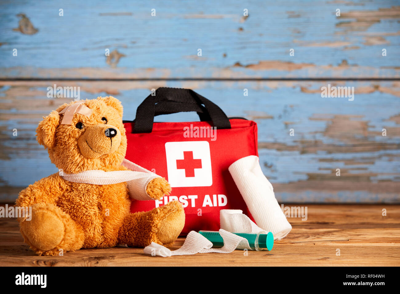 L intervento di primo soccorso e di emergenza sanitaria concetto con un colorato di rosso kit medici a fianco di un grazioso piccolo orsacchiotto con braccio bendato in una imbracatura su rustico Foto Stock