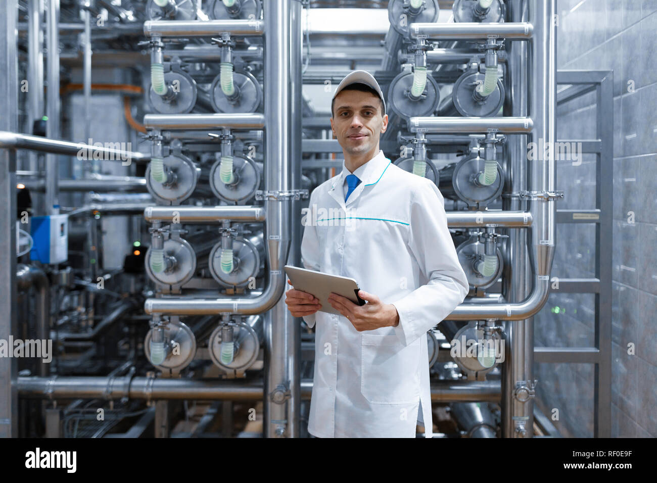 Uomo in una veste bianca con una compressa nelle sue mani è nel negozio di produzione in fabbrica Foto Stock