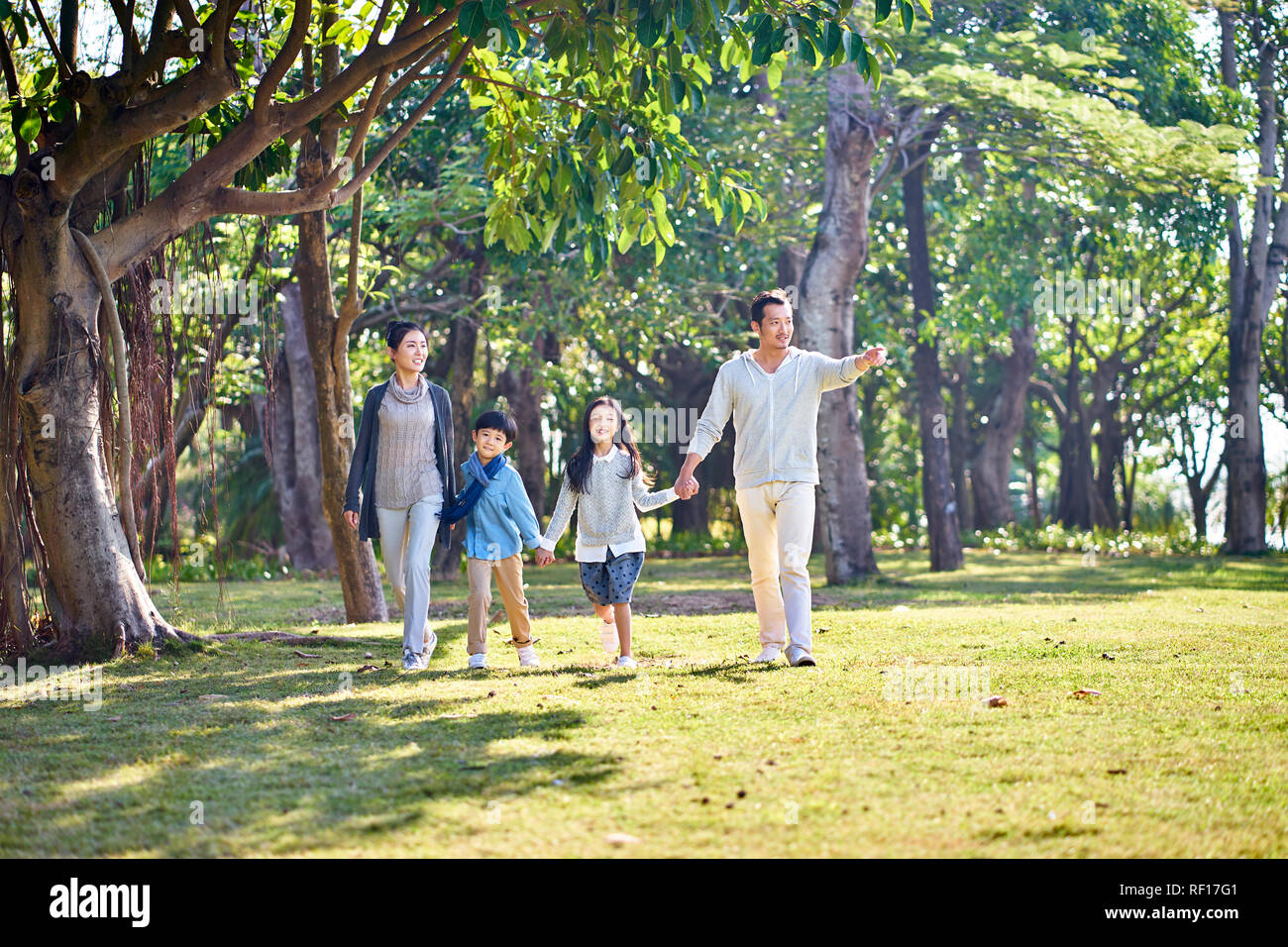 Famiglia asiatica con due figli che camminano mano nella mano all'aperto nel parco. Foto Stock