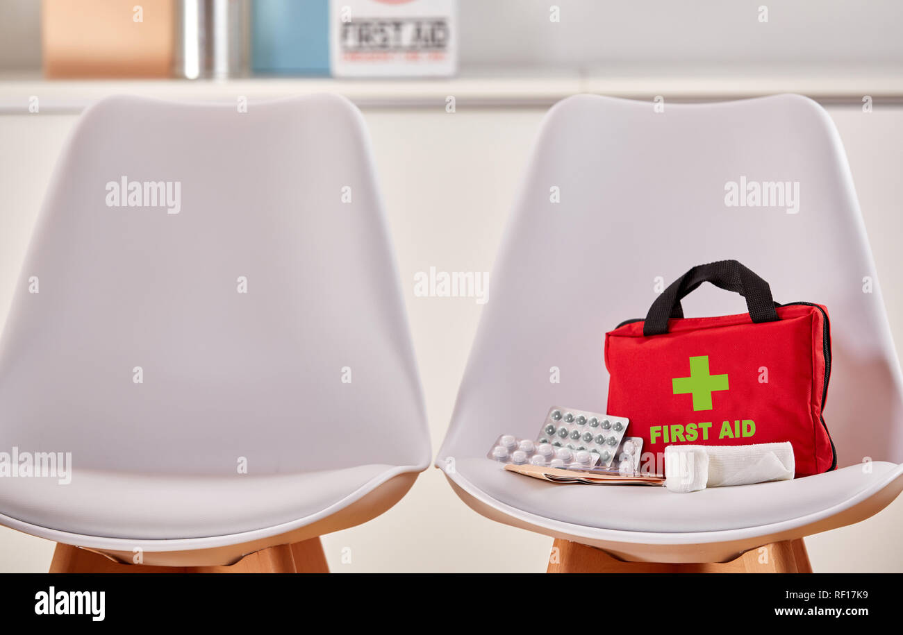 Kit di primo soccorso come concetto per la cura della salute accanto a una sedia vuota nella sala di attesa di un ospedale o di un centro medico Foto Stock