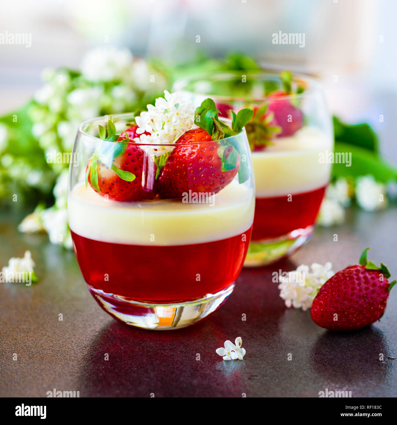 Dolce italiano Panna cotta con fragole e fiori in vetro sul cartone grigio Foto Stock