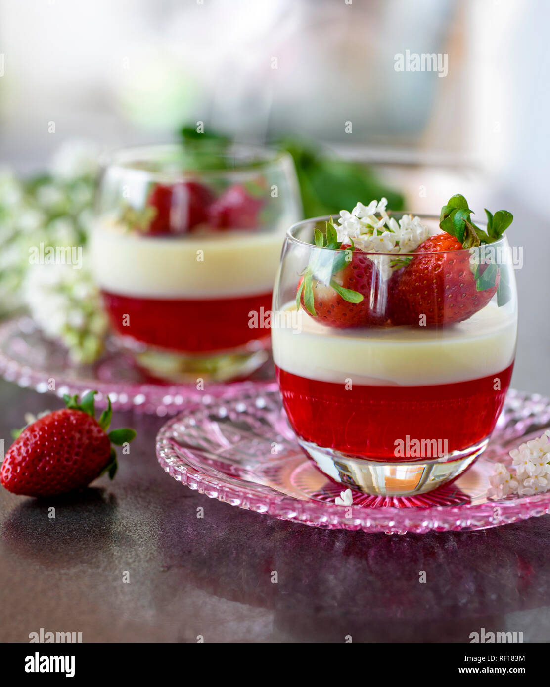 Dolce italiano Panna cotta con fragole e fiori in vetro sul cartone grigio Foto Stock