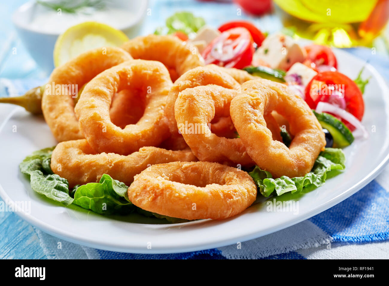 Croccante fritti golden anelli di totano con una fresca insalata greca in una vista ravvicinata su una piastra Foto Stock